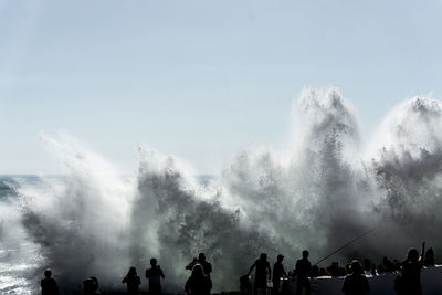 People looking at waterfall against sky