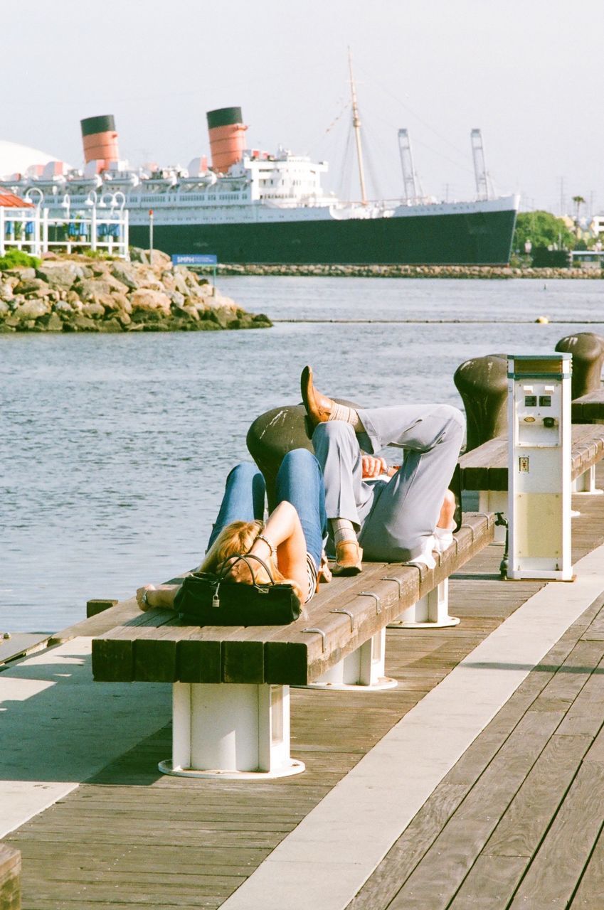 water, built structure, architecture, building exterior, lifestyles, leisure activity, rear view, men, railing, pier, sitting, person, river, full length, sky, nautical vessel, clear sky