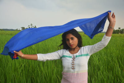 Woman with arms raised on field against blue sky