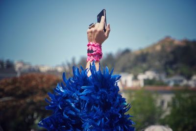 Close-up of a woman holding her arm up against a blue sky with blue feathered sleeves 