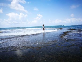 Rear view of woman standing in sea against sky