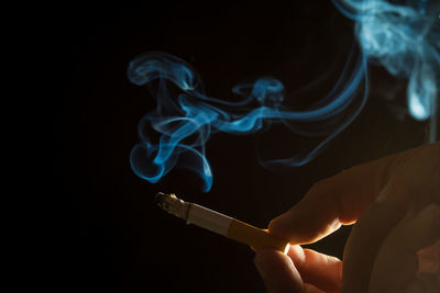 Close-up of human hand holding cigarette against black background