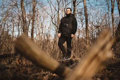 A young bearded man posing in an all black casual outfit on a tree trunk