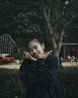 Portrait of smiling young woman against trees