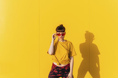 Mid adult woman wearing sunglasses in front of yellow wall during sunny day