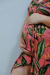 Midsection of pregnant woman with hands on stomach against white background