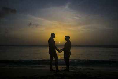 Silhouette friends on beach against sky during sunset