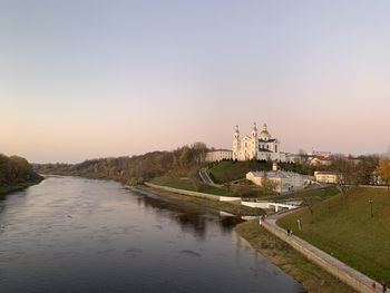 Bridge over river by buildings against sky during sunset