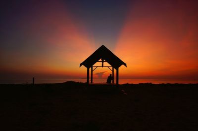 Silhouette lifeguard hut on field against sky during sunset