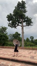 Rear view of woman walking by trees against sky