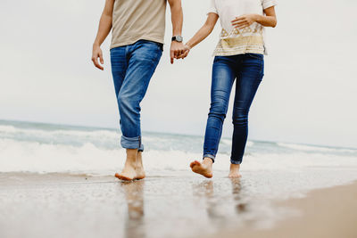 Low section of couple holding hands while walking at beach
