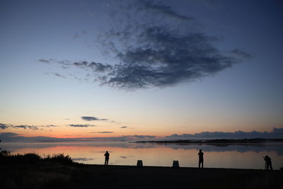 Silhouette people standing on beach against sky during sunset