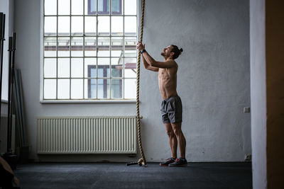 Full length of shirtless man standing against window