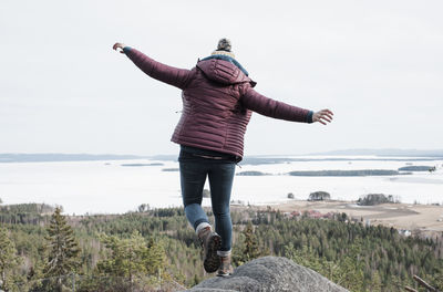 Woman jumping off a rock whilst hiking with a view of the ocean