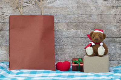 Close-up of shopping bag with teddy bear and christmas gift against wooden wall