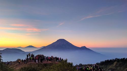 People on mountain range against sky during sunset