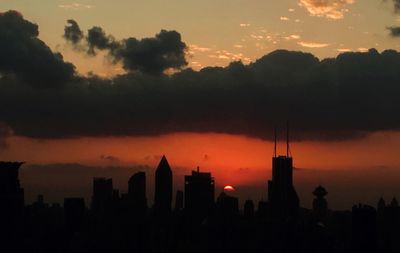 Silhouette of city against cloudy sky during sunset