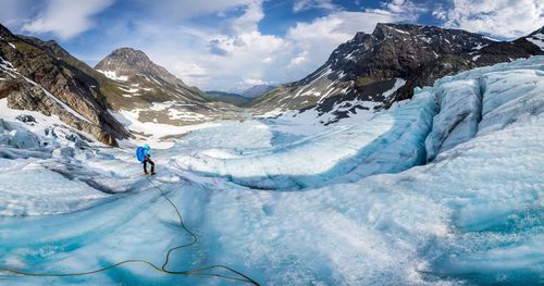 Person standing on snow covered mountains against cloudy sky