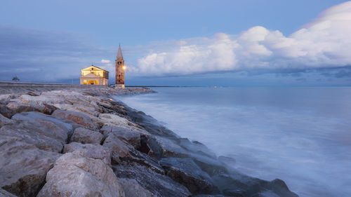 Lighthouse amidst sea and buildings against sky