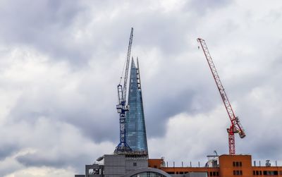 Low angle view of crane by building against sky