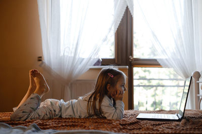 Child watching cartoons on laptop. serious kid with technology at home on bed spending time on-line