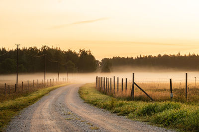 Road amidst field against sky during sunset