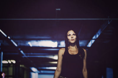 Woman looking away while standing in illuminated parking lot