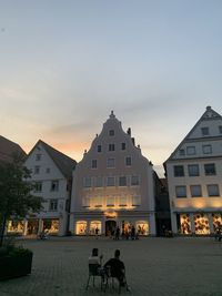 People on street amidst buildings against sky at dusk