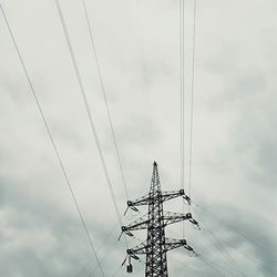 Low angle view of electricity pylon against cloudy sky