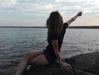 Rear view of woman sitting on shore against sky