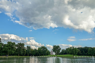 Lake by trees at park against cloudy sky