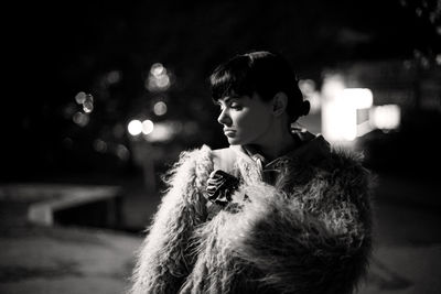 Mid adult woman wearing fur coat while standing in city at night