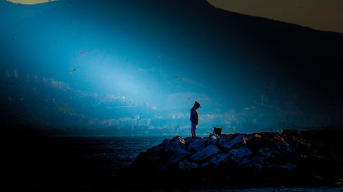 Silhouette man standing on rock by sea against blue sky