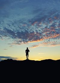 Silhouette man standing on landscape against sky during sunset