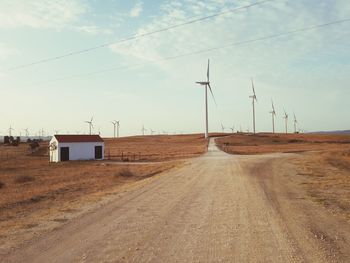 Road leading towards windmills against sky