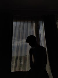 Silhouette man looking through window at home
