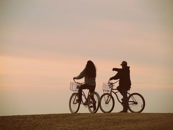 Silhouette people on bicycle against sky during sunset