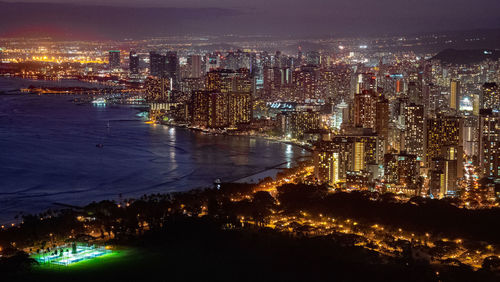 High angle view of illuminated city by sea against sky at night