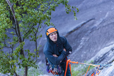 Man being bored belaying climber while hanging from granite wall cold