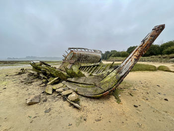 Damaged boat on beach against sky