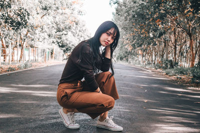 Young woman looking away while sitting on road in city