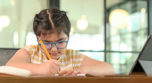 Cropped shot of asian child girl with glasses is studying at home with serious expression.