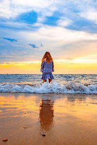 Rear view of girl standing on shore at beach against sky