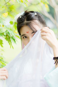 Portrait of young woman covering face with white fabric