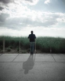 Rear view of man standing on field against sky