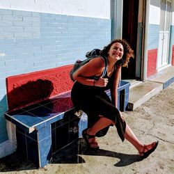 Full length of young woman sitting on bench smiling 