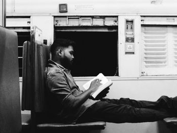 Side view of young man reading book