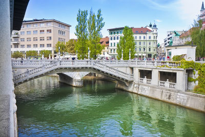 Arch bridge over river by buildings in city against sky