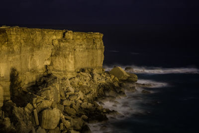 Rocks on beach against sky at night