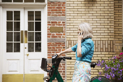 Side view of mature woman using smart phone against building